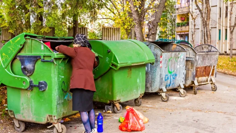 Une femme âgée en situation de précarité fouille dans une benne à ordures, illustrant la pauvreté au Portugal